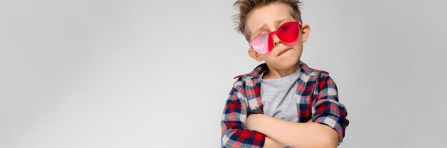 Un chico guapo en una camisa a cuadros, camisa gris y pantalones vaqueros se encuentra en gris