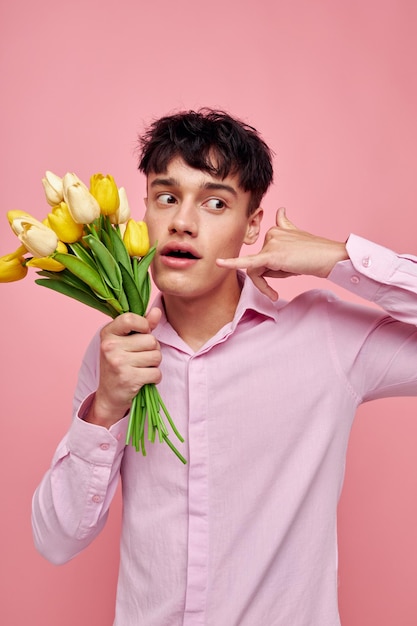 Chico guapo en una camisa rosa con un ramo de flores gesticulando con sus manos fondo aislado inalterado