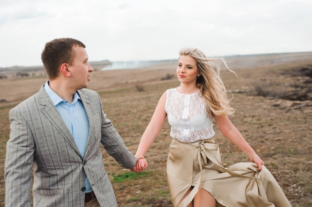 Chico guapo y chica rubia caminando por el campo, un hombre lleva a una mujer de la mano.