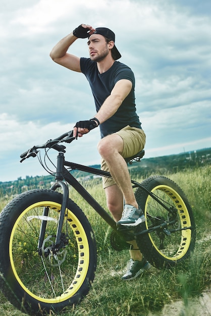 Chico guapo con estilo en bicicleta en las montañas y mira la vista inferior lejana