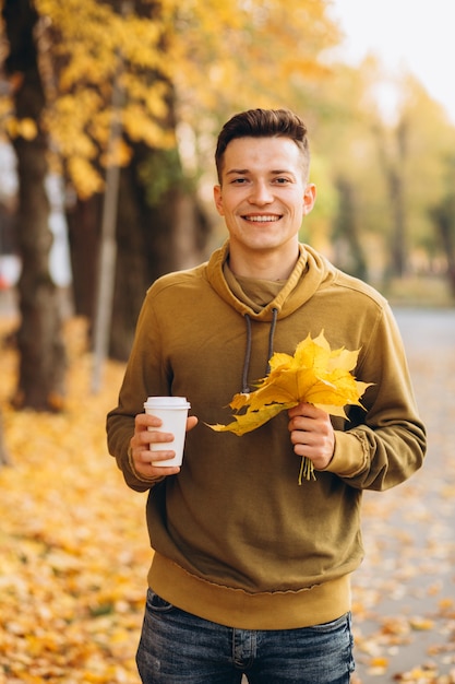 Chico guapo y feliz con un ramo de hojas amarillas sonriendo y tomando café