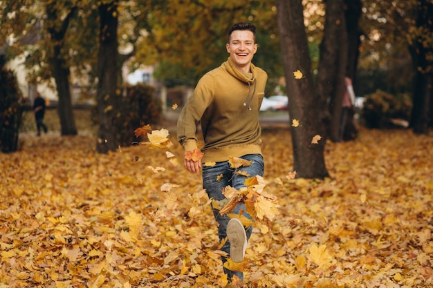 Chico guapo y feliz sonríe y corre esparciendo hojas amarillas en el parque de otoño