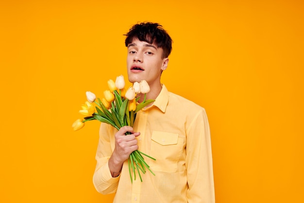 Chico guapo en gafas amarillas con un ramo de flores fondo amarillo inalterado