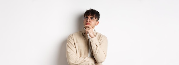 Chico guapo hipster con gafas se ve pensativo en el espacio vacío tocando la barbilla y frunciendo el ceño.