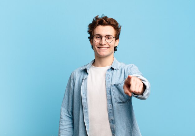 Chico guapo joven apuntando al frente con una sonrisa satisfecha, confiada y amistosa, eligiéndote