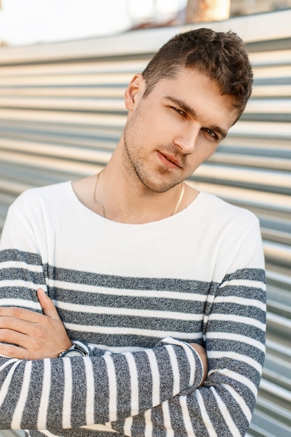 Chico guapo joven con barba en un suéter de moda se encuentra cerca de la pared de metal