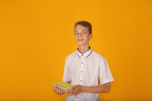 Un chico guapo joven con una camisa blanca tiene cuadernos en sus manos fondo amarillo