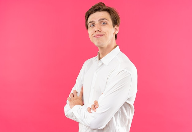 Chico guapo joven complacido con camisa blanca cruzando las manos aisladas en la pared rosa con espacio de copia