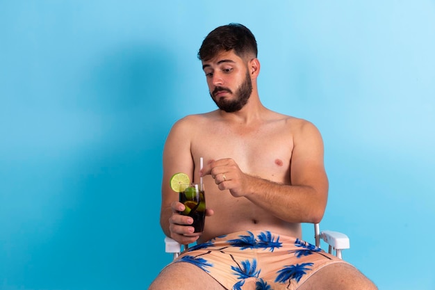 Chico guapo joven disfrutando de las vacaciones de verano bebiendo refrescos de cola fría El hombre está de vacaciones sentado en la silla de playa tomando una copa