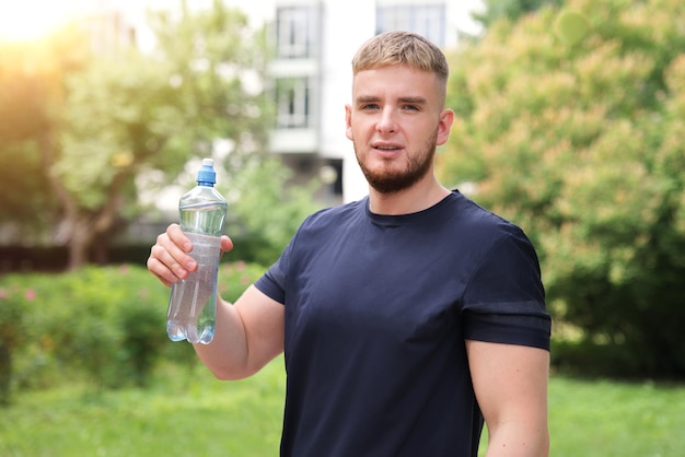 un chico guapo, joven, feliz, sediento, corredor, está bebiendo agua pura y fresca de una botella de plástico