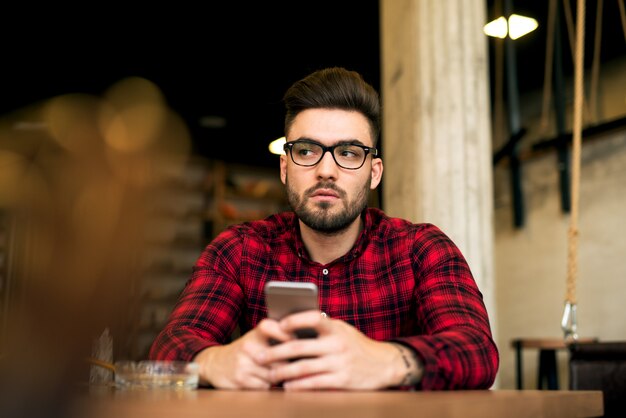 Chico guapo joven inconformista con barba y gafas sentado en un café.