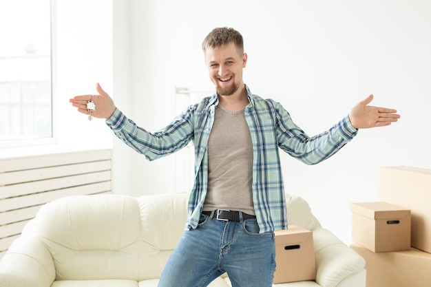 Chico guapo joven muestra las llaves de su nuevo apartamento mientras está de pie en la sala de estar. Hipoteca