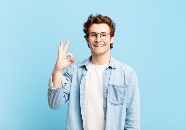 Chico guapo joven que se siente feliz, relajado y satisfecho, mostrando aprobación con gesto bien, sonriendo