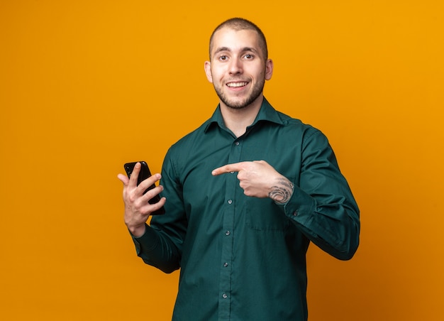 Chico guapo joven sonriente con camisa verde sosteniendo y puntos en el teléfono