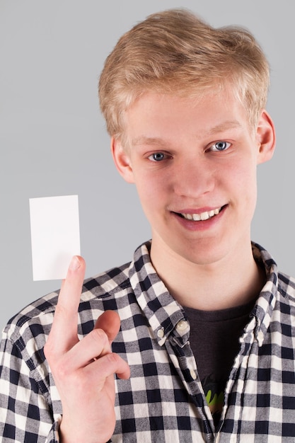 Chico guapo joven sosteniendo una tarjeta en blanco