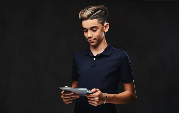 Chico guapo joven vestido con una camiseta negra con una tableta. Aislado en el fondo oscuro.