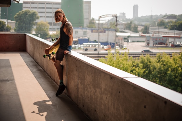 Chico guapo de pelo largo sentado en el parapeto con longboard