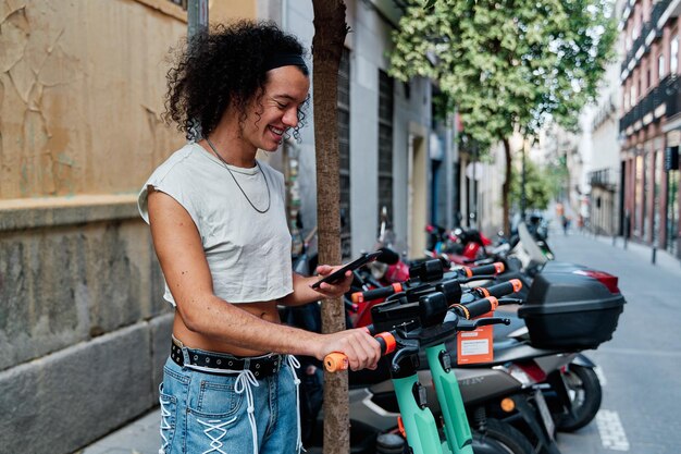 Un chico guapo y satisfecho usa el transporte urbano ecológico alquila un scooter usando su teléfono