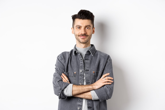 Chico guapo seguro en traje casual cruzan los brazos en el pecho, sonriendo complacido, profesional de pie sobre fondo blanco.