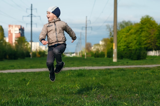 Chico guapo de seis años jugando, saltando, corriendo, sonriendo en el parque.
