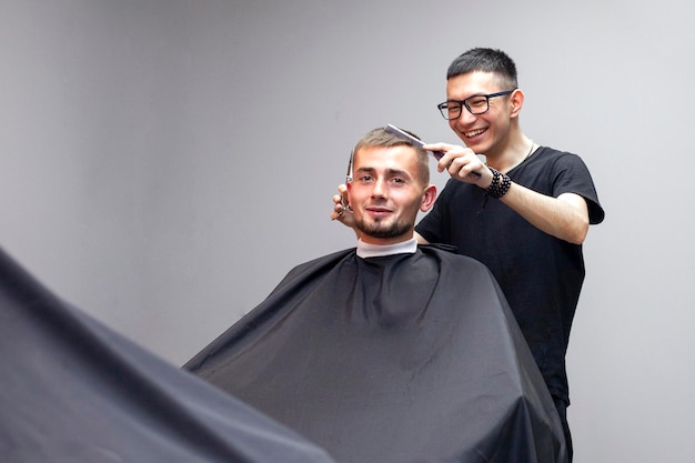 Chico guapo tiene un corte de pelo en la peluquería un joven peluquero kazajo corta manualmente con tijeras