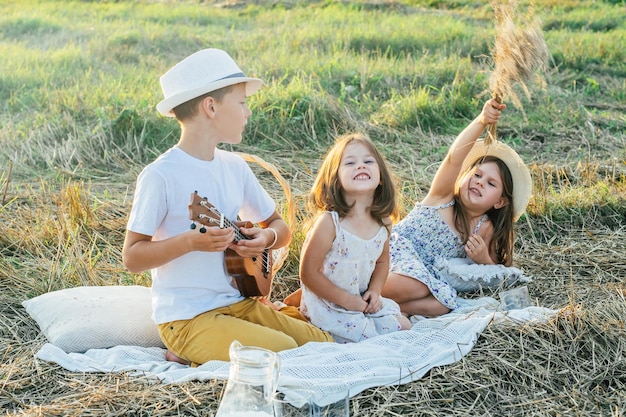 Chico guapo toca el ukelele sentado en una manta en el campo entre hierba cortada en seco Retrato de niños descansando en la hierba