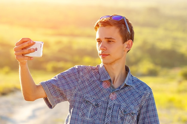 chico guapo toma una selfie en el teléfono en el sol