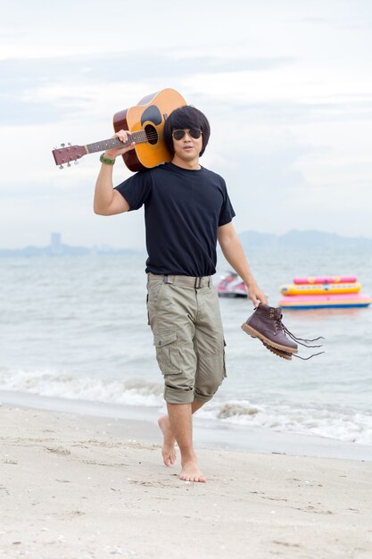 Chico con guitarra de pie en la playa, pantalones de carga