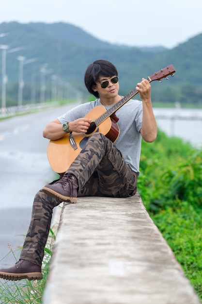 Chico con guitarra de pie en la presa, pantalones de carga