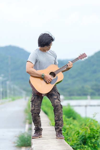 Chico con guitarra de pie en la presa, pantalones de carga