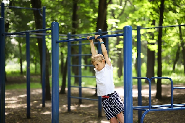 El chico va a hacer deporte en el parque colgado de la barra horizontal y se balancea