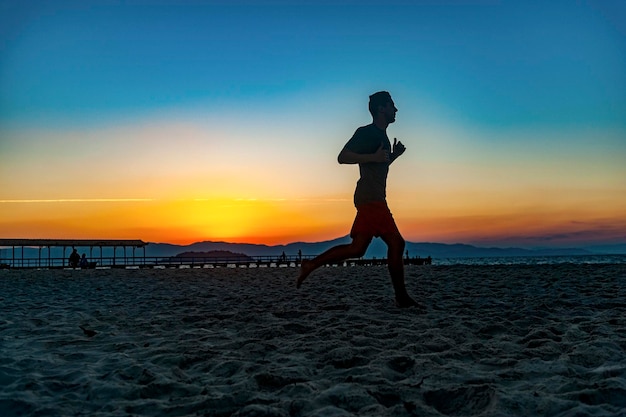 Chico haciendo deporte con pelota en la playa en pleno atardecer de verano en la costa brasileña