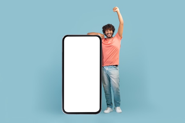 Chico hindú emocional posando con una gran maqueta de teléfono celular
