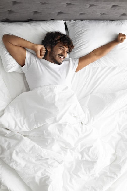 Foto chico hindú feliz estirándose en la cama por la mañana