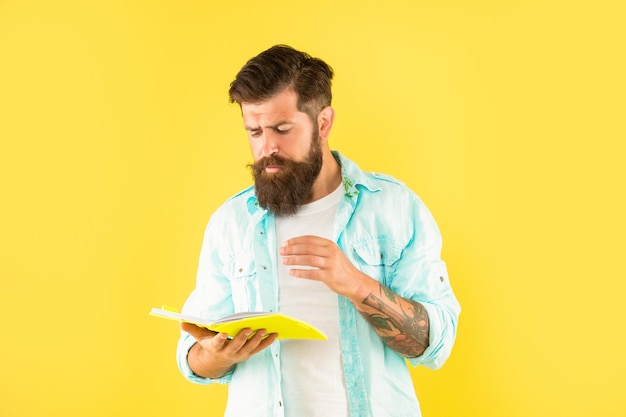 Chico hipster concentrado leyendo cuaderno en lector de fondo amarillo