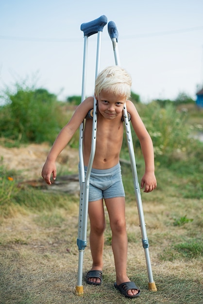 Chico hombre sin camisa de pie con muletas al aire libre