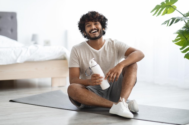 Chico indio positivo bebiendo agua mientras hace ejercicio