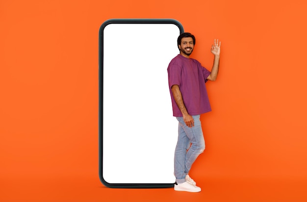 Chico indio positivo posando junto a un teléfono enorme con pantalla blanca