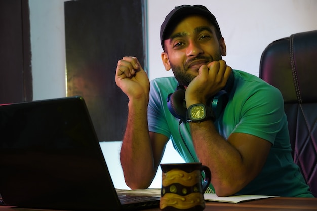 Chico indio sonriente con ordenador portátil trabajando o estudiando en línea