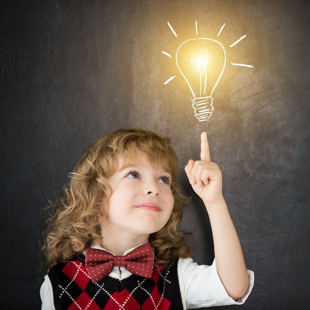 Foto chico inteligente en clase. niño feliz contra la pizarra. bombilla de luz de dibujo. concepto de idea