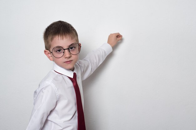 Chico inteligente con gafas y uniforme escolar escribiendo a bordo. concepto de escuela intermedia. copia espacio