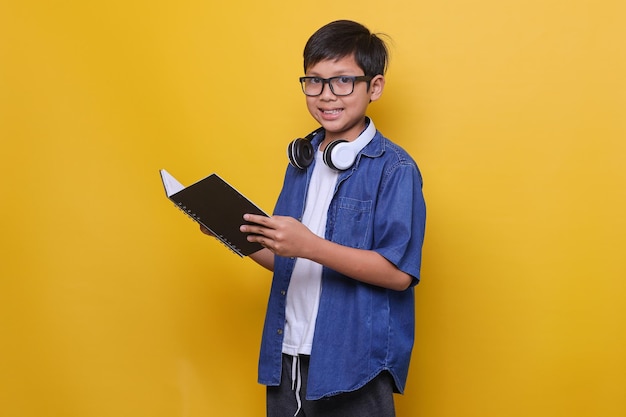 Chico inteligente con ropa informal, auriculares y anteojos sosteniendo un libro y sonriendo a la cámara sobre ti