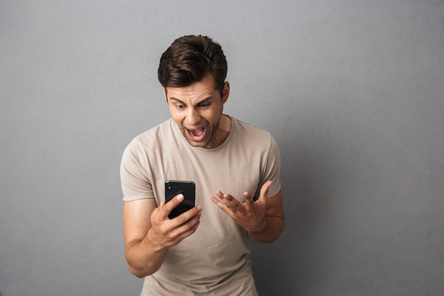 Chico irritado con camiseta gritando de ira mientras mira el teléfono inteligente