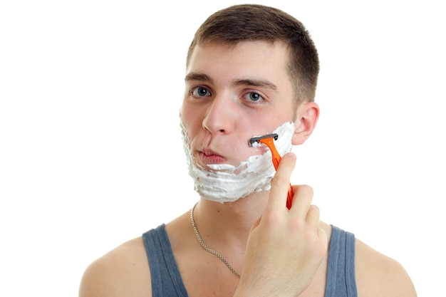 Foto chico joven se afeita la cara con espuma de afeitar de cerca aislado en la pared blanca