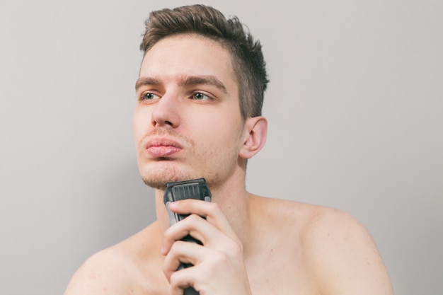 Foto chico joven se afeita con una maquinilla de afeitar eléctrica