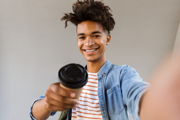 Chico joven alegre de pie afuera sosteniendo selfie haciendo café