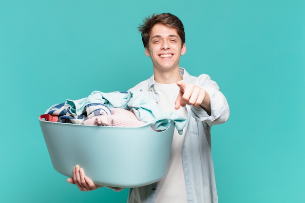 Chico joven apuntando al frente con una sonrisa satisfecha, confiada y amistosa, eligiéndote lavar la ropa concepto