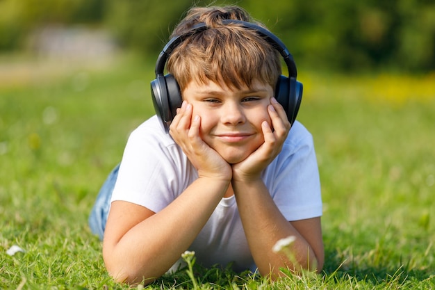 Chico joven con auriculares escuchando música tumbado en el césped del parque