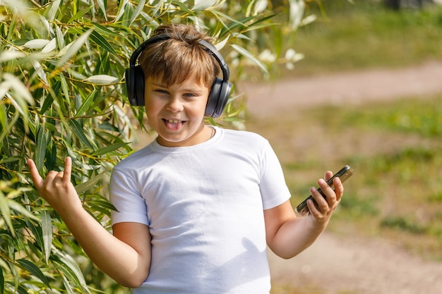 Chico joven en auriculares con smartphone escucha música en el parque de verano