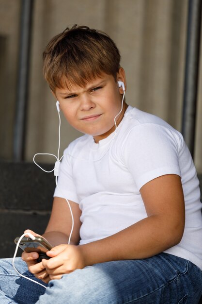 Chico joven en auriculares con smartphone escucha música en el parque de verano